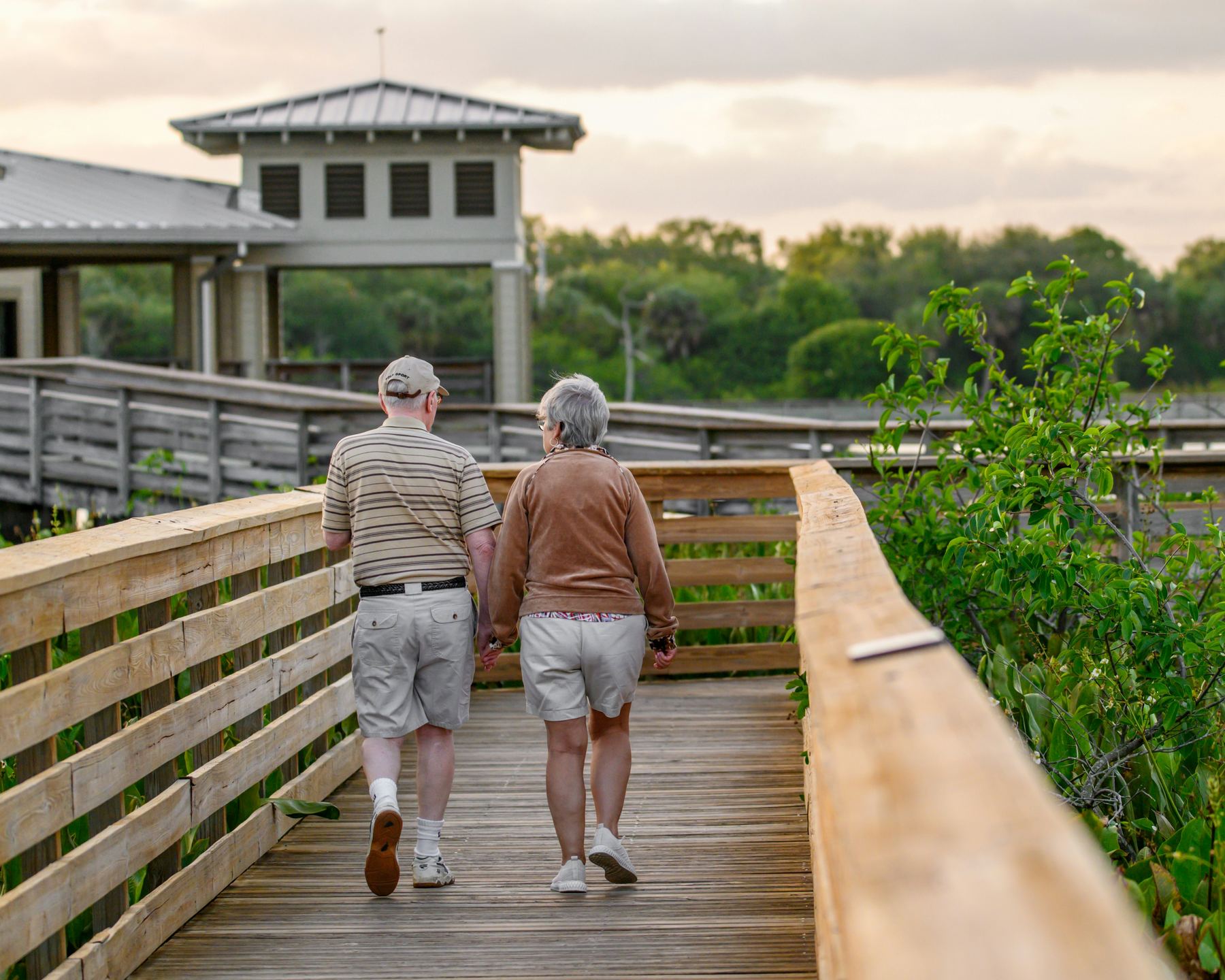 A retired couple walking together outdoors on a boardwalk